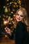 Portrait of young attractive celebrating woman holding sparkles. Background of christmas tree