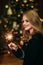 Portrait of young attractive celebrating woman holding sparkles. Background of christmas tree