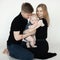 Portrait of young attractive family in dark clothes with plump cherubic baby infant toddler sitting on white background.