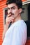 Portrait of young attractive mustache man in T-shirt dreamily looking in camera on street