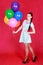 Portrait of a young attractive woman holding bunch of many bright balloons