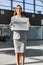 Portrait of young attractive woman standing while holding white board with welcome signage in arrival area at airport