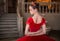 Portrait of young ballerina in a red tutu and crown from back, face turned in profile against the background of vintage interior