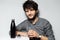 Portrait of young bearded guy with disheveled hair, holding glass of water near black stainless thermal bottle.