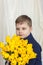 Portrait of a young, beautiful boy. Holds a huge armful of fresh yellow tulips. The concept of spring and holiday, March 8,