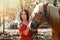 Portrait of Young beautiful brunette woman in red dress posing near horse. Sunlight