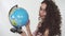 Portrait young beautiful curly girl with creative make up twisting globe with fun and pretty smile. Girl stops the globe