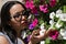 Portrait of a young, beautiful, dark and South American woman with a printed shirt and sunglasses, smelling flowers of different
