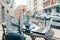 Portrait of young beautiful fashionable blond woman in warm clothes sitting in an outdoor cafe with laptop computer, drinking cup