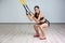 Portrait of young beautiful fit woman in sportswear doing a squat exercise with fitness straps in the gym. TRX functional training