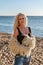 Portrait of a young beautiful gentle blonde in jeans with a black T-shirt and a white fur jacket on a sandy beach in the rays of t