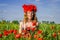 Portrait of a young beautiful girl in a poppy field with a wreath of poppies on her head on a hot summer sunny day