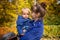 Portrait of a young beautiful mother holds a toddler in her arms and kisses him gently in autumn park. mom`s love