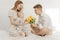 Portrait of young beautiful mother sitting, kneeling, holding little plump baby and handsome father presenting bouquet.