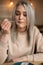 Portrait of young beautiful pleased woman with cute make-up holding fork with piece of cake, sitting at table in cafe.