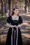 Portrait of a young, beautiful woman in a black medieval dress standing in a pine forest. Attractive girl in a gothic dress.