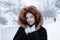 Portrait of young beautiful woman with blue eyes in black faux fur coat with red hood on a walk in winter snowy park