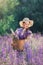 Portrait of young beautiful woman with bouquet of flowers in basket at sunny field. Pretty vintage girl in lilac dress and hat