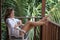 Portrait of young beautiful woman freelancer drinking coffee from white cup on balcony of tropical bungalow with palm trees view