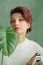 Portrait of a young beautiful woman with perfect smooth skin with a large green tropical leaf. Fashion, beauty, makeup