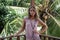 Portrait of young beautiful woman in pink dress on balcony of tropical bungalow with palm trees view