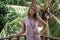 Portrait of young beautiful woman in pink dress on balcony of tropical bungalow with palm trees view