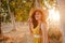 Portrait of young beautiful woman wearing a yellow dress walking by a path of trees. Summertime and lifestyle