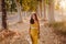 Portrait of young beautiful woman wearing a yellow dress walking by a path of trees. Summertime and lifestyle