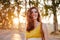 Portrait of young beautiful woman wearing a yellow dress walking by a path of trees. Summertime and lifestyle