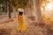 Portrait of young beautiful woman wearing a yellow dress walking by a path of trees. Summertime and lifestyle. Back view