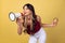 Portrait of young beuatiful girl, student in casual style clothes shouting at megaphone isolated on yellow studio