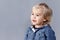 Portrait of a young blond boy on gray background. A three years boy looks into the distance