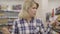 Portrait of young blond caucasian woman walking along shelves with alcohol and thinking. Concentrated pretty lady