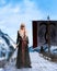 Portrait of a young blonde haired viking warrior woman standing on a pier holding a sword with a long boat behind iin winter. 3D