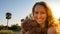 Portrait of a young blonde woman with curly hair looking at the camera with a big smile during the golden hour -