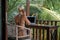 Portrait of young blonde woman freelancer working with laptop on balcony of tropical bungalow with palm trees view