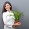 Portrait of young botanist woman in uniform holding plant against gray background