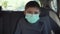 Portrait of young boy in medical protective mask sitting on back seat near car window at city traffic during quarantine