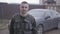 Portrait of young brave military man staying and smiling on the street in uniform on the background of car.