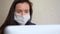 Portrait of young brunette business woman entrepreneur in protective medical face mask using laptop, writing notes at home