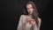 Portrait of young brunette long-haired caucasian girl attentively watching into smartphone on black background.