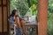 Portrait of young brunette woman freelancer working with laptop on balcony of tropical bungalow with palm trees view