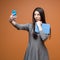 Portrait of a young business woman in grey dress with blue smartphone and a tablet making a selfie and looking on the phone