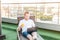 Portrait of Young businessman with drink working on laptop comfortably sitting on deckchair on office terrace with Urban Landscape