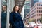 Portrait of young businesswoman in a blue coat, against big city background