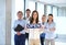 Portrait of young businesswoman holding open sign with team behind at office