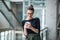 A portrait of young businesswoman with smartphone standing in corridor outside office.