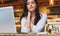 Portrait of young businesswoman, student, dressed in white blouse, sitting at table in cafe in front of computer.