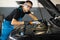 Portrait of young caucasian man in blue overalls and safety glasses inspects engine with flashlight. Male car mechanic