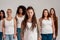 Portrait of young caucasian tattooed woman with dreadlocks in white shirt looking at camera. Group of diverse women